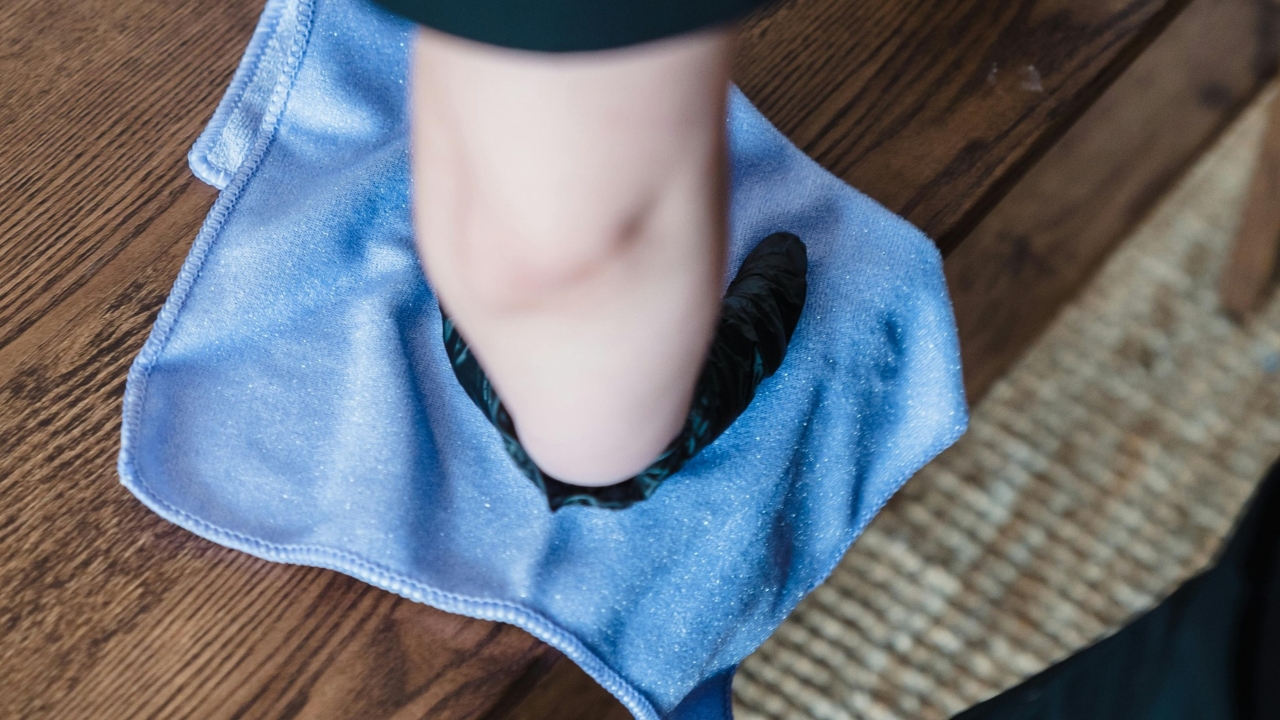 Photographie d'une main dans un gant de ménage en latex qui nettoie une table avec une lingette microfibres