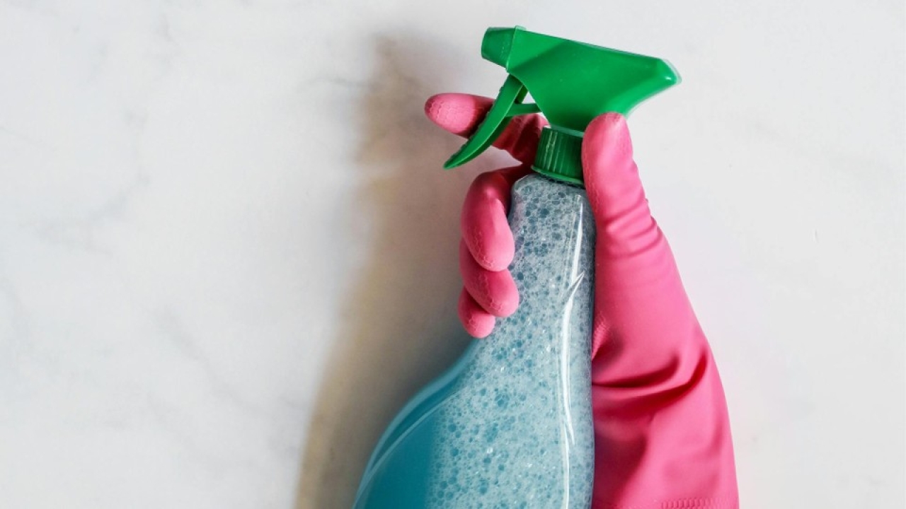 Photographie d'une main dans un gant en latex qui tient un produit ménager au format spray