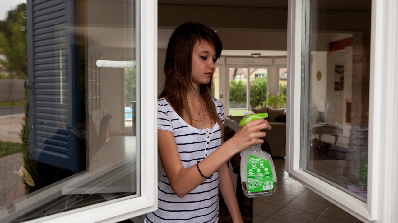 Photographie d'une jeune femme qui pulvérise un produit pour nettoyer les vitres de ses fenêtres.