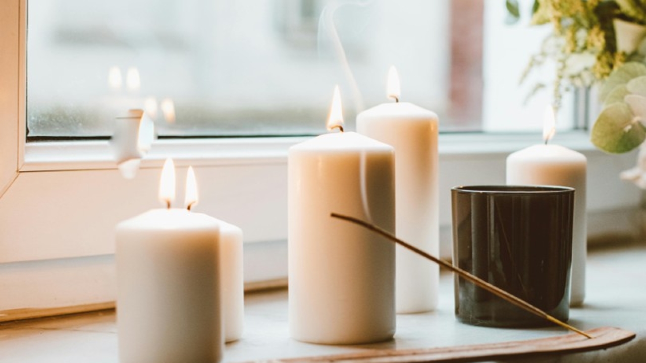 Photographie de plusieurs bougies et d'un baton d'encens qui se consumment avec émission de fumée