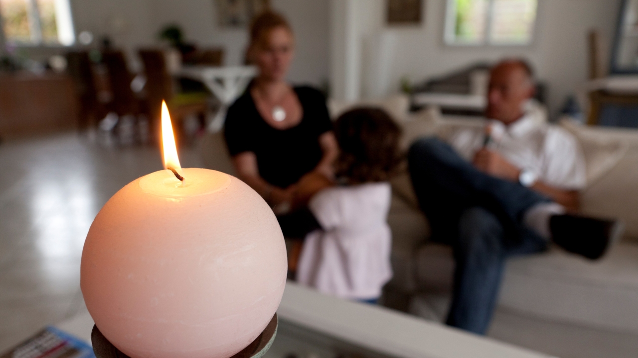 Photographie d'une bougie allumée dans le salon d'un couple avec son enfant