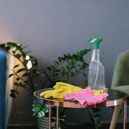 Photographie d'un produit ménagers en format spray avec des gants en caoutchouc sur une table basse d'un salon