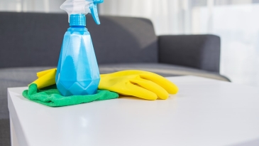 Un produit d'entretien en spray sur une table basse avec un gant et un chiffon