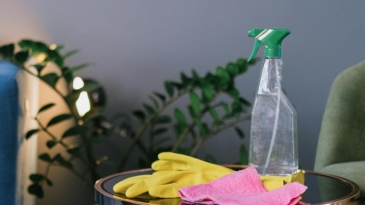 Photographie d'un produit ménagers en format spray avec des gants en caoutchouc sur une table basse d'un salon